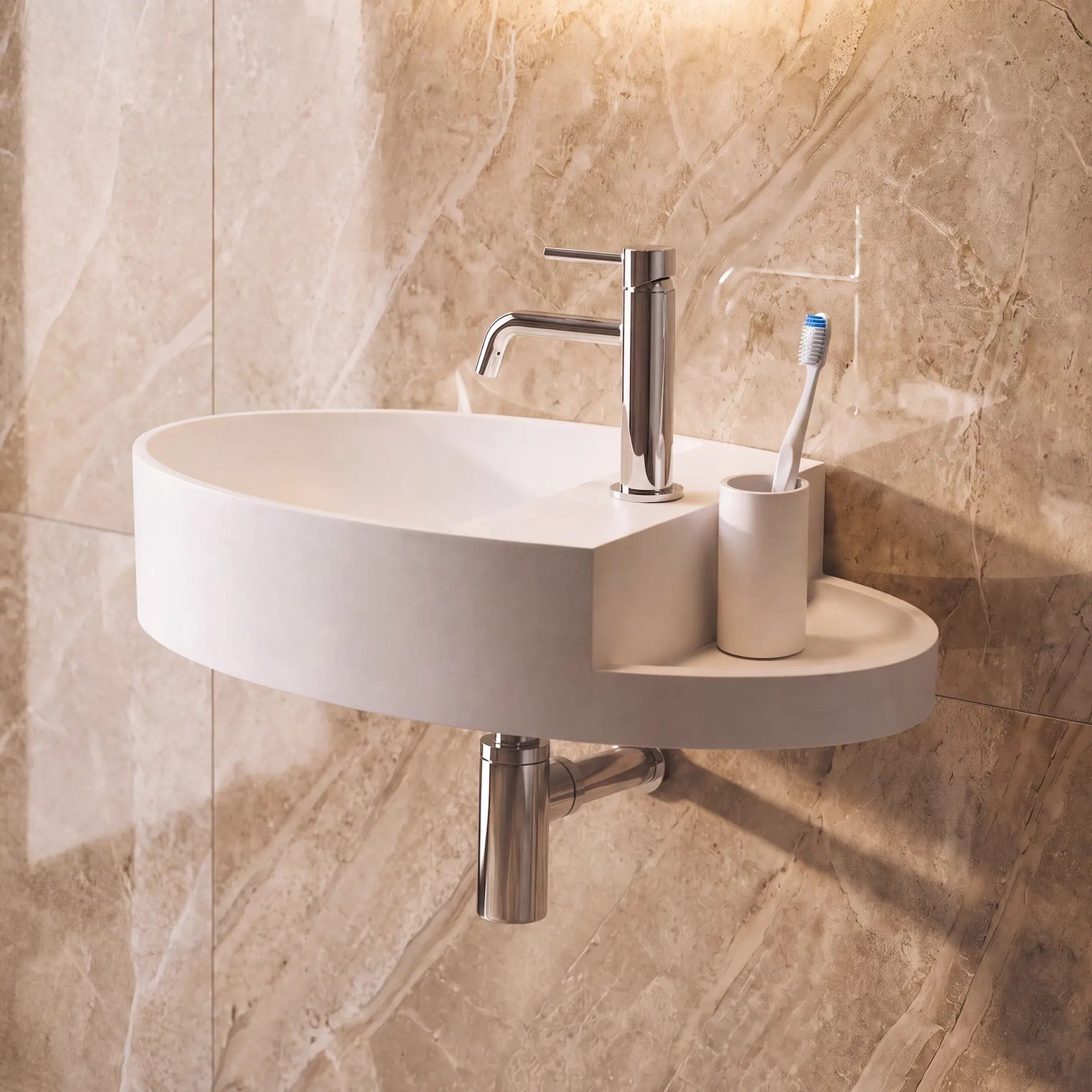 A modern wall-mounted oval bathroom sink in white, paired with a polished chrome faucet, toothbrush holder, and toothbrush, set against a beige marble-look tiled wall.