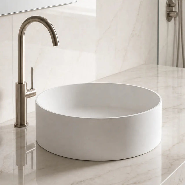Modern bathroom with a round solid surfaces white sink and bronze faucet on a marble countertop.