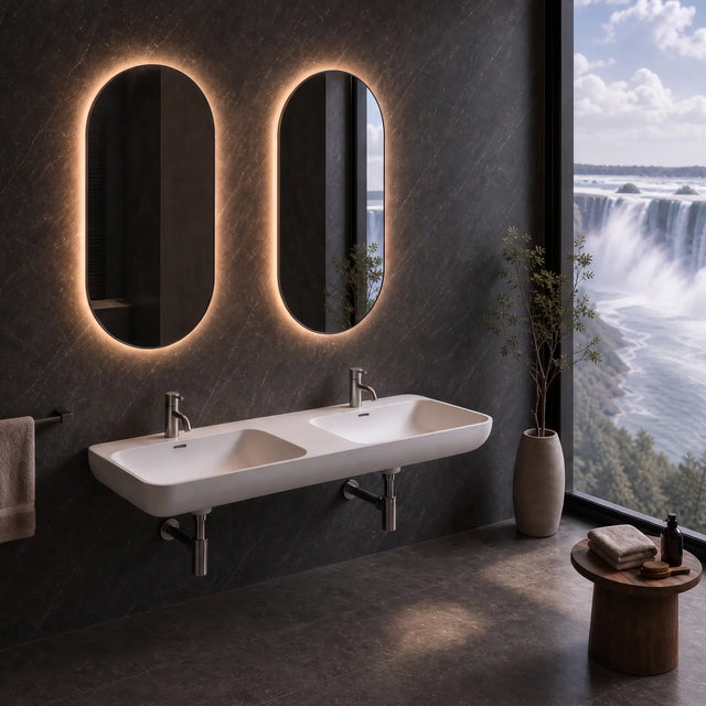 A modern double-sink bathroom wall setup with two illuminated oval mirrors, a white floating basin, chrome faucets, a towel bar, and a large window overlooking a waterfall landscape.