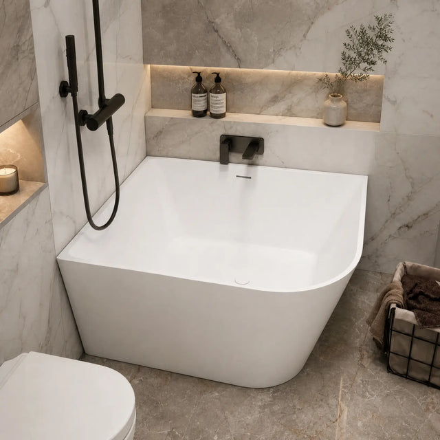 A modern freestanding bathtub in a marble-look bathroom with black fixtures, built-in shelves with toiletries, and a basket of towels nearby.