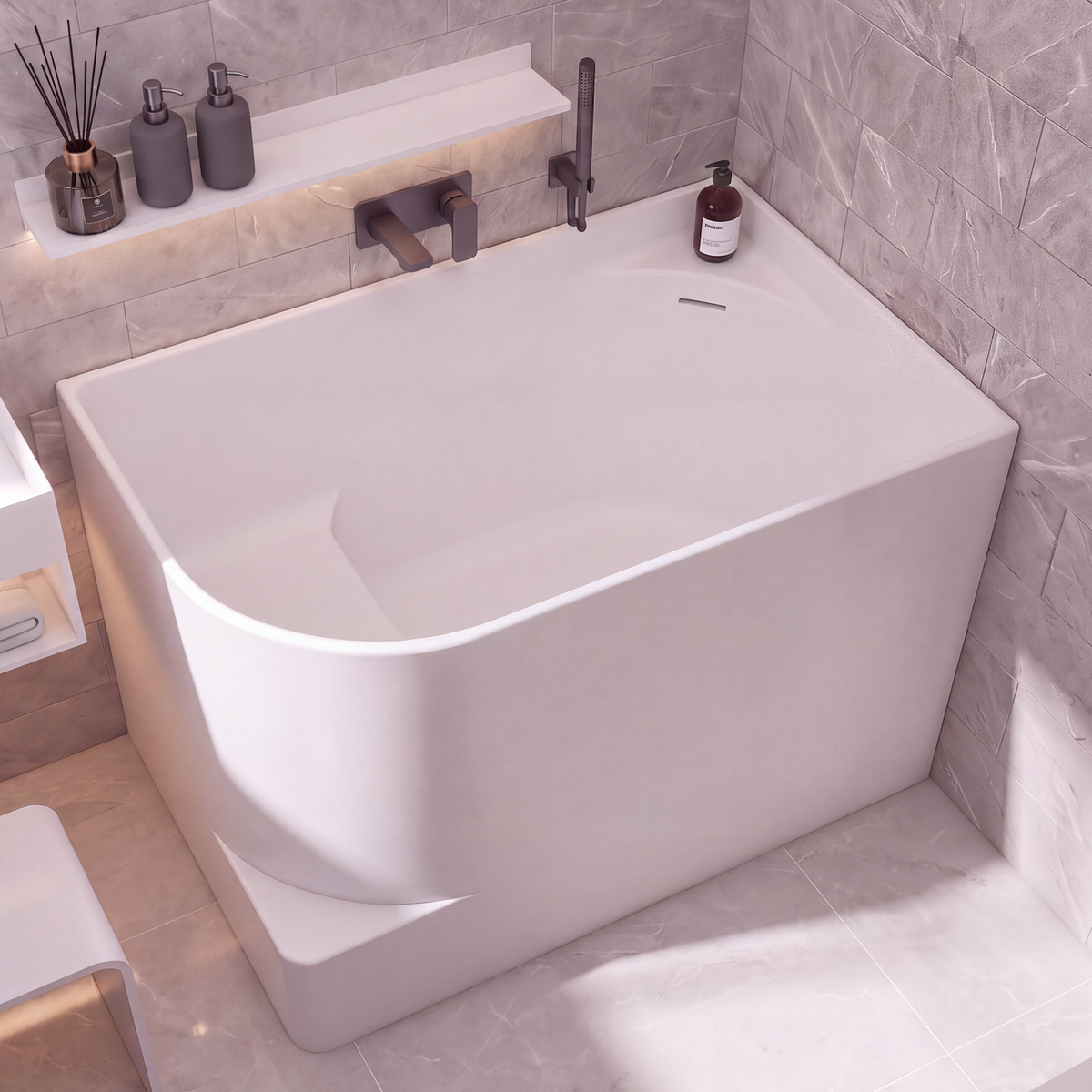 A modern freestanding bathtub in a minimalist bathroom setting with gray marble-look tiled walls and floor, a white vanity, and a small white stool.