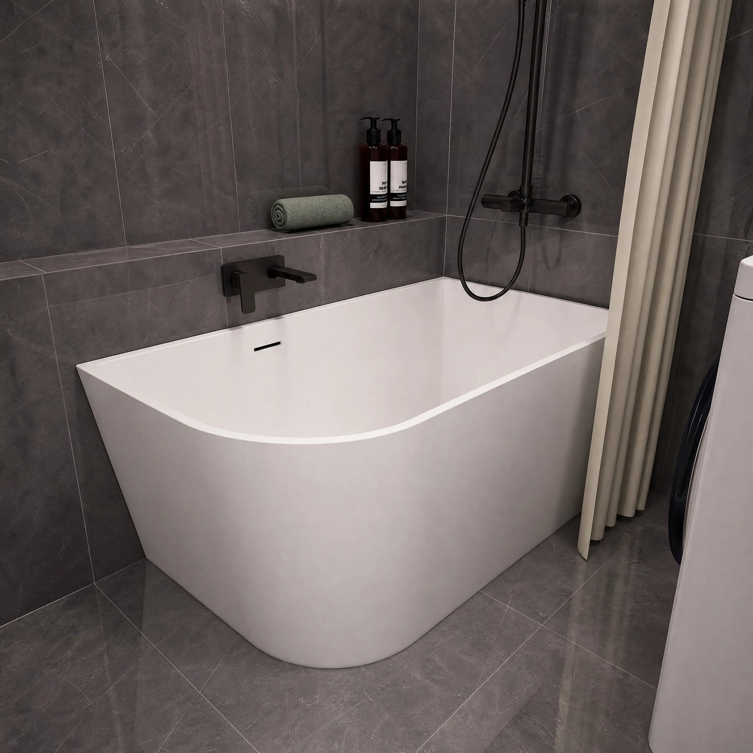 A modern freestanding bathtub with a curved corner design, shown installed in a bathroom with dark gray tiled walls and floor. The tub is white with matte black fixtures, including a wall-mounted faucet and shower system.