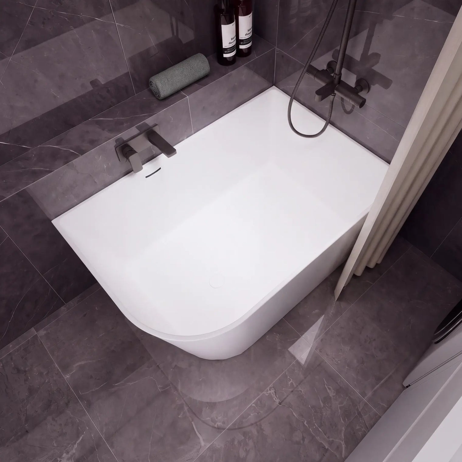 A modern white freestanding bathtub with a dark gray tiled bathroom setting, featuring a wall-mounted chrome faucet, a handheld shower attachment, and a beige curtain on the left.