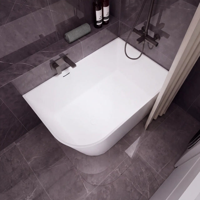 A modern white freestanding bathtub with a dark gray tiled bathroom setting, featuring a wall-mounted chrome faucet, a handheld shower attachment, and a beige curtain on the left.