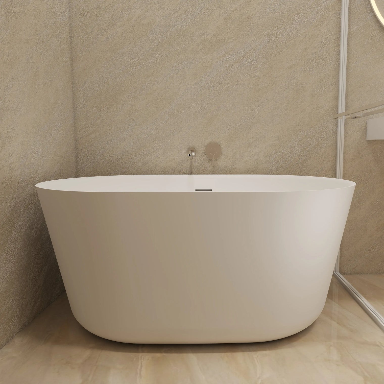 A modern freestanding oval bathtub in matte white, set in a minimalist bathroom with beige stone walls and floor, next to a glass shower screen.