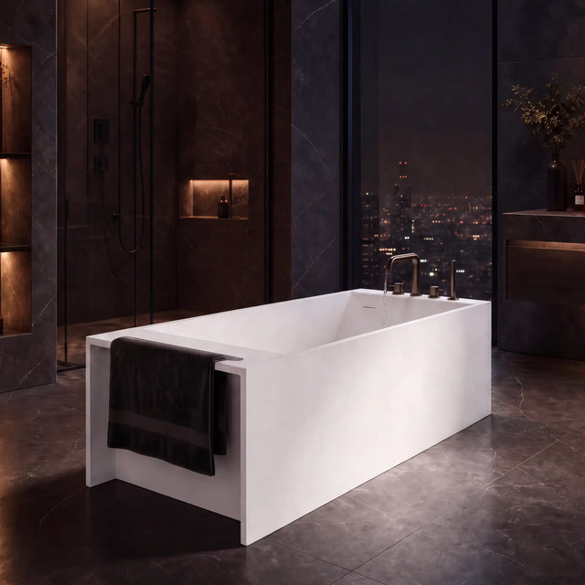 A modern freestanding rectangular bathtub in matte white, shown in a luxurious dark-toned bathroom with a city skyline visible through large windows at night.