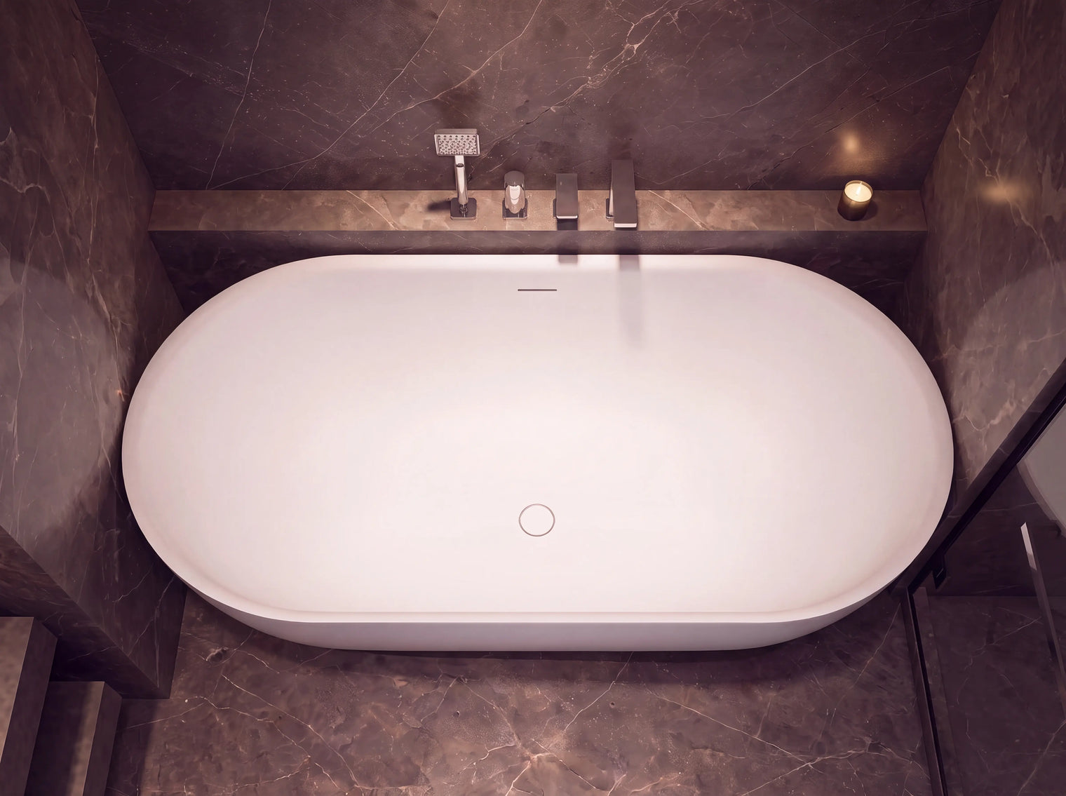 A freestanding oval bathtub in white, set into a dark marble-tiled bathroom with a built-in shelf holding a chrome faucet and shower head.