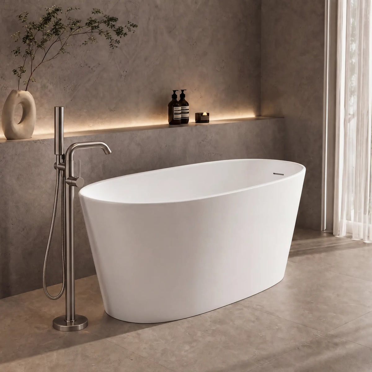 A modern freestanding oval bathtub in matte white, shown in a minimalist bathroom setting with a chrome floor-mounted faucet, textured gray walls, and a large window with sheer curtains.