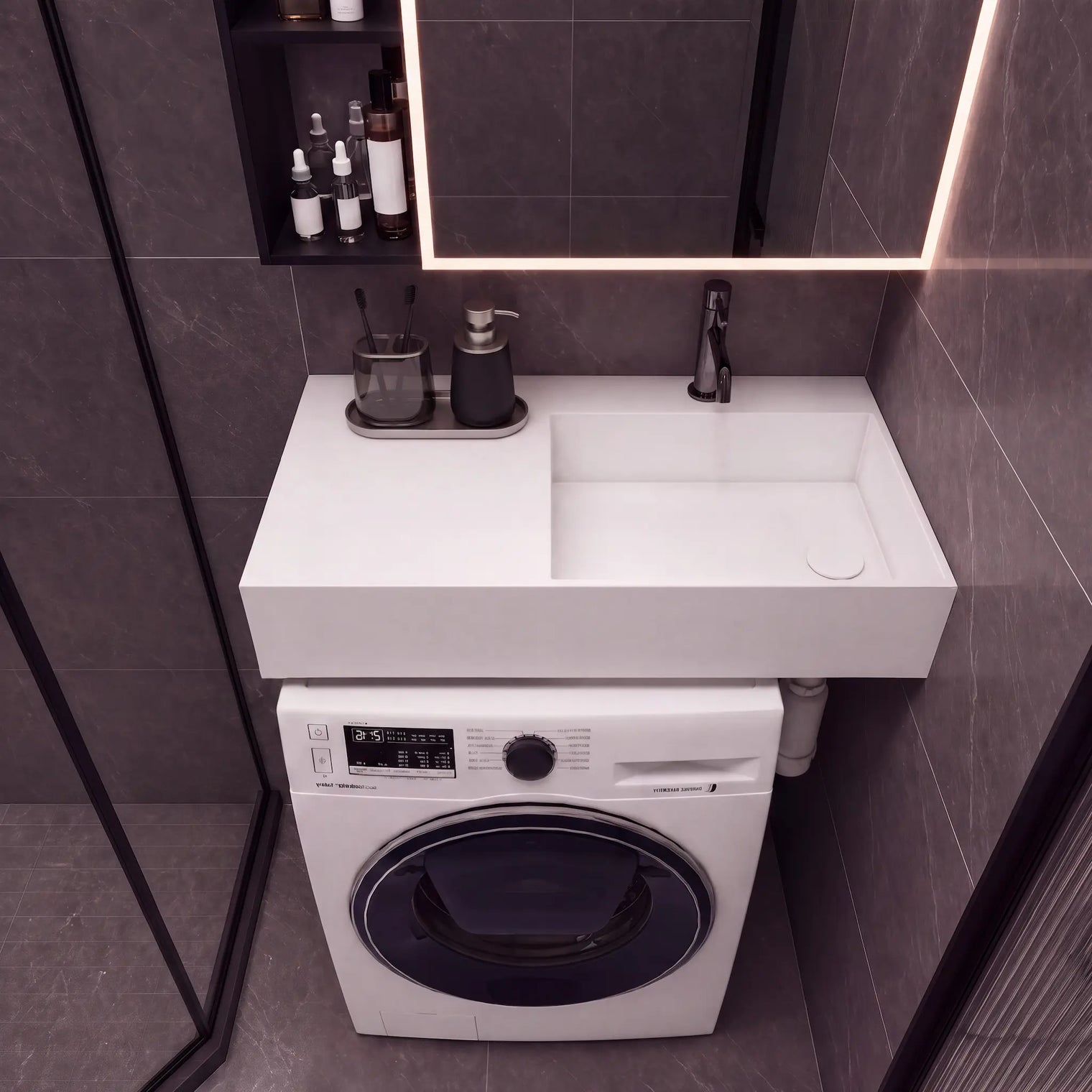 A modern bathroom setup featuring a white rectangular sink countertop with a matte black faucet, integrated into a white front-loading washing machine. The unit is set against dark gray tiled walls under a black-framed mirror with warm lighting.
