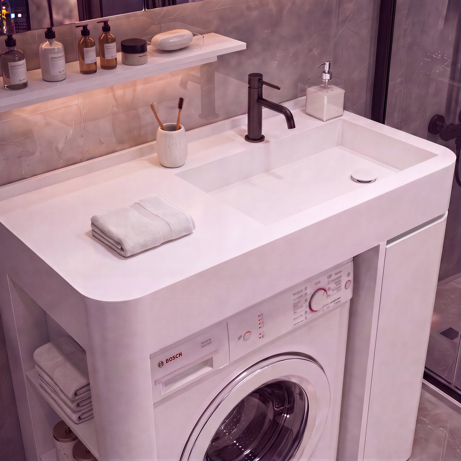 A white integrated washing and sink vanity unit in a modern bathroom, featuring a Bosch front-loading washing machine beneath a double basin sink with a matte black faucet. The unit is styled with folded towels, toiletries on a shelf, and a glass shower enclosure in the background.
