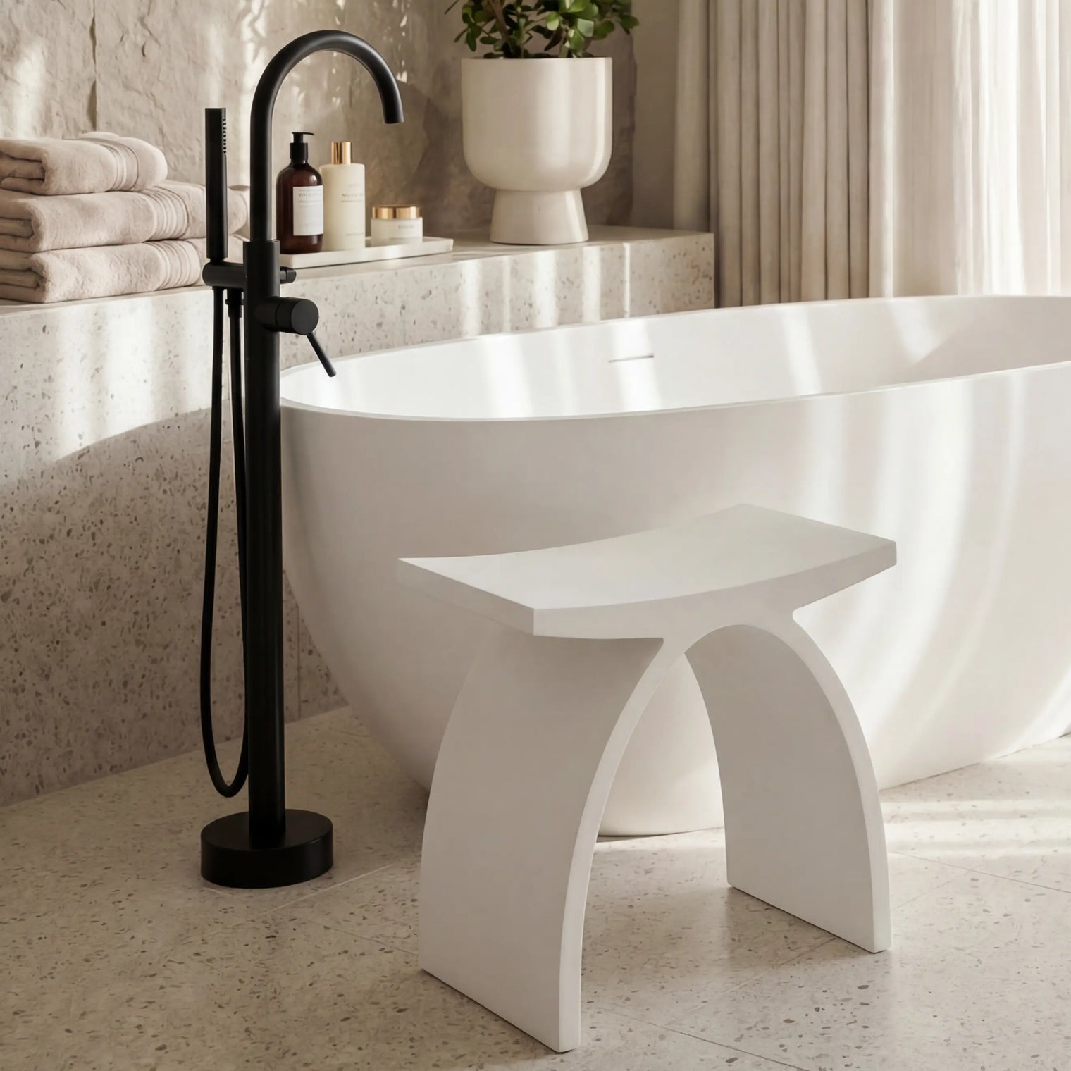 Modern bathroom with a freestanding bathtub, black faucet, and decorative plants.