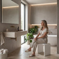 Woman sitting on a stool in a modern bathroom with neutral tones.