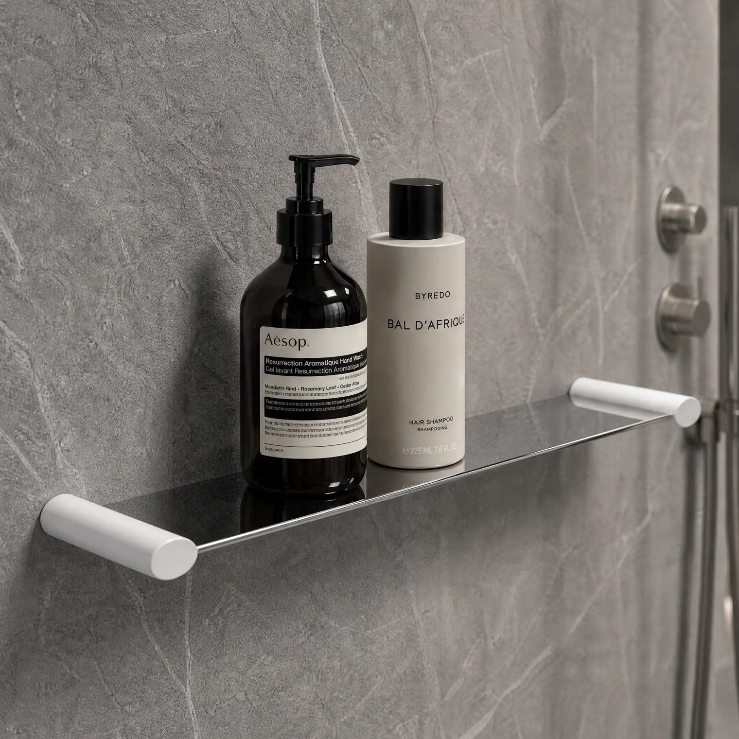 Bathroom shelf with Aesop products against a gray tiled wall.
