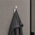 Gray towel hanging on a white hook against a gray wall.