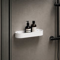 White shower caddy with bottles on a gray wall with a black shower head.