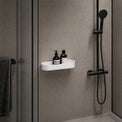 Shower setup with a white shelf holding bottles against a gray wall.