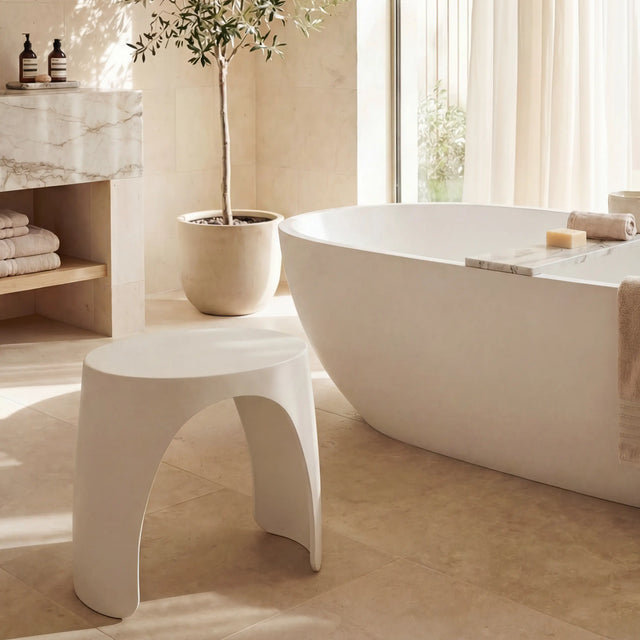 Modern bathroom with a freestanding bathtub, stool, and decorative plant.
