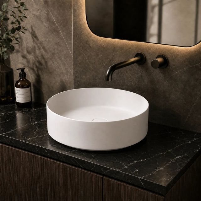 White round sink on a dark marble countertop with a mirror and bottles in the background.