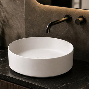White round sink on a dark marble countertop with a mirror and bottles in the background.