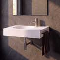 A modern wall-mounted white sink with a chrome faucet, set against dark gray marble-look tiled walls in a bathroom. A rectangular mirror is mounted above the sink, and a dark brown towel hangs from the side.