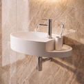 A modern wall-mounted oval bathroom sink in white, paired with a polished chrome faucet, toothbrush holder, and toothbrush, set against a beige marble-look tiled wall.