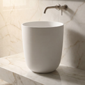 White freestanding sink on a marble countertop with a neutral-toned wall in the background