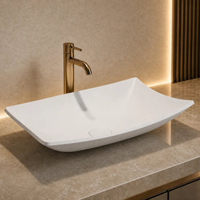 White rectangular Solid Surfaces sink on a gray countertop with a gold faucet in a modern bathroom setting.