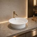 White round sink with gold faucet on a marble countertop in a bathroom setting.