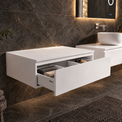 A modern floating bathroom vanity in matte white, shown installed against a dark marble wall. The vanity features a rectangular top with an open drawer pulled out to reveal folded towels, and a second drawer partially visible behind it.