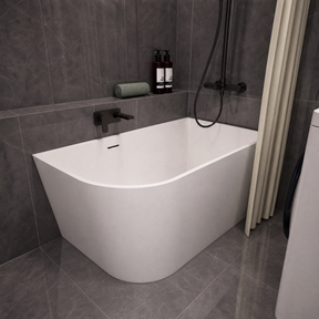 A modern freestanding bathtub with a curved corner design, shown installed in a bathroom with dark gray tiled walls and floor. The tub is white with matte black fixtures, including a wall-mounted faucet and shower system.