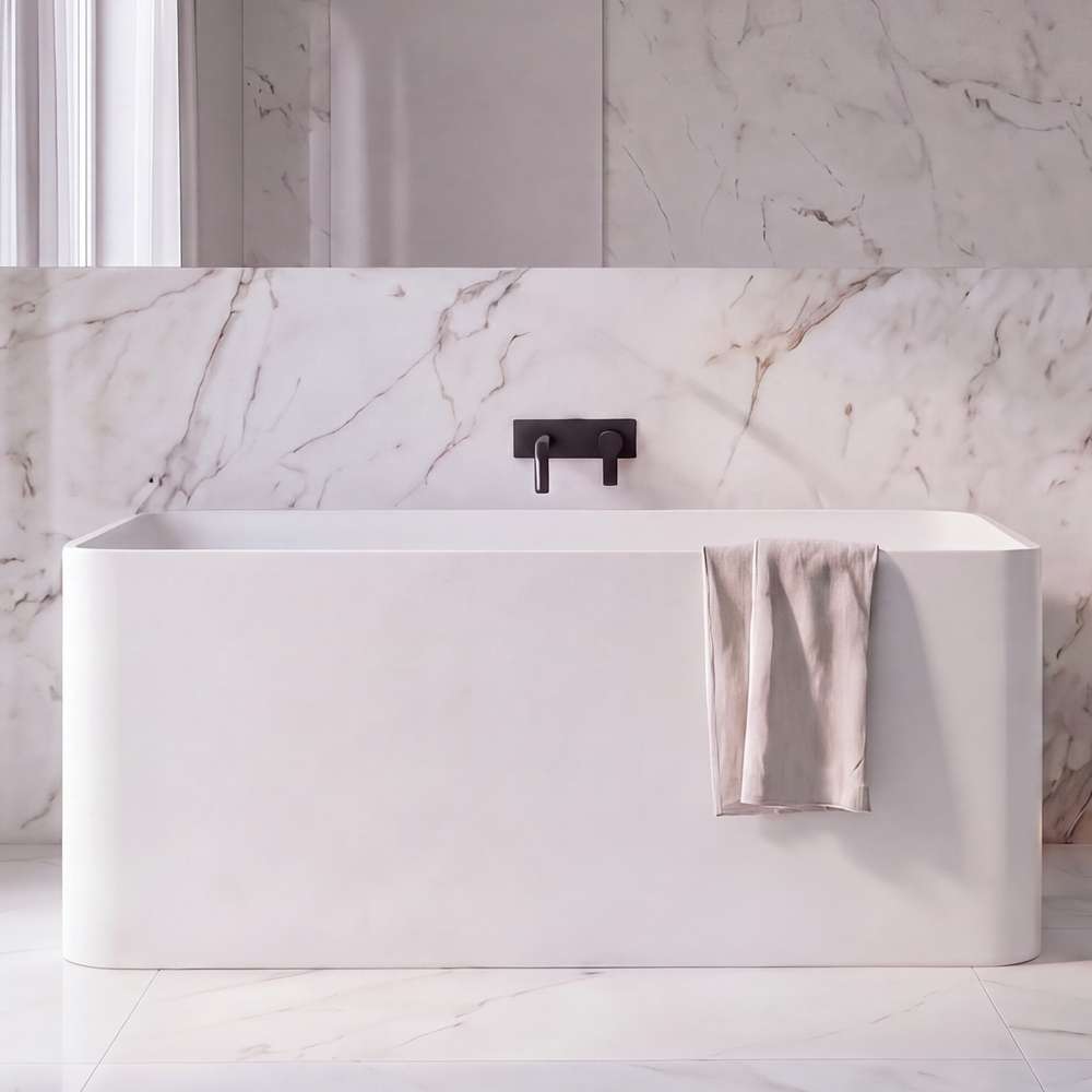 A modern bathroom interior with a white freestanding bathtub, a matching white vanity cabinet with integrated sink, marble-look wall and floor, black faucet fixtures, sheer curtains, and a mirror.