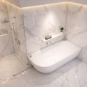 A modern freestanding bathtub in a bright marble-tiled bathroom with a glass shower door and built-in shelf.