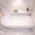 A modern freestanding white bathtub set in a bright bathroom with white marble walls and floor, featuring a built-in shelf with a small plant and soap dispenser.