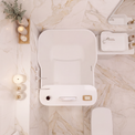 An overhead view of a modern white wall-mounted bathtub with a built-in control panel, set against a beige marble tiled bathroom wall with decorative candles and a small plant.