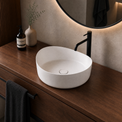 White solid surfaces sink on a wooden vanity with a black faucet and decorative items.