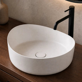 White solid surfaces sink on a wooden vanity with a black faucet and decorative items.