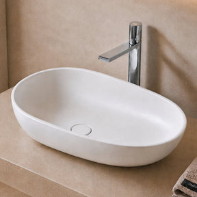 Modern bathroom with a white solid surfaces sink on a beige countertop, illuminated by warm lighting.