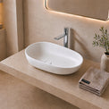 Modern bathroom with a white Solid Surfaces sink on a beige countertop, illuminated by warm lighting.