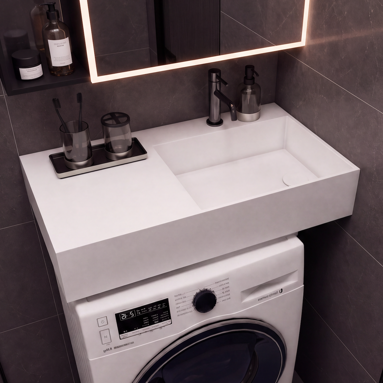 A modern bathroom vanity setup with a white integrated sink and washing machine cabinet, set against dark gray tiled walls under a lit mirror.