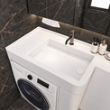 A white integrated sink vanity unit with a built-in washing machine, shown in a modern bathroom setting with dark marble wall and floor tiles.