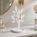 A white leaf-shaped jewelry tree stand with a round base, styled on a marble bathroom counter with gold jewelry displayed on its branches.