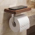 Wooden shelf with a smartphone and toilet paper holder mounted on a tiled bathroom wall.