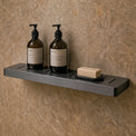 Bathroom with shower setup, bottles on a shelf, and mirror reflecting the room.