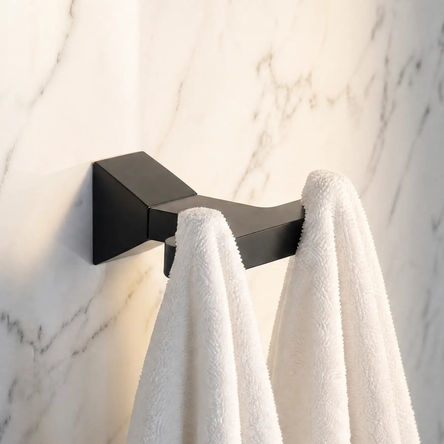 Black towel hook with white towels on a marble wall