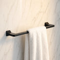 Black towel rack with a white towel against a marble wall.
